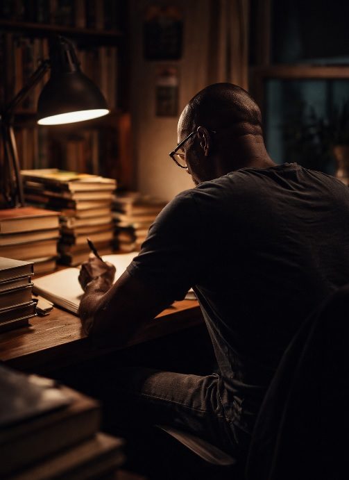 Author seen from behind writing manuscripts at night, symbolizing reflection, aging, and storytelling